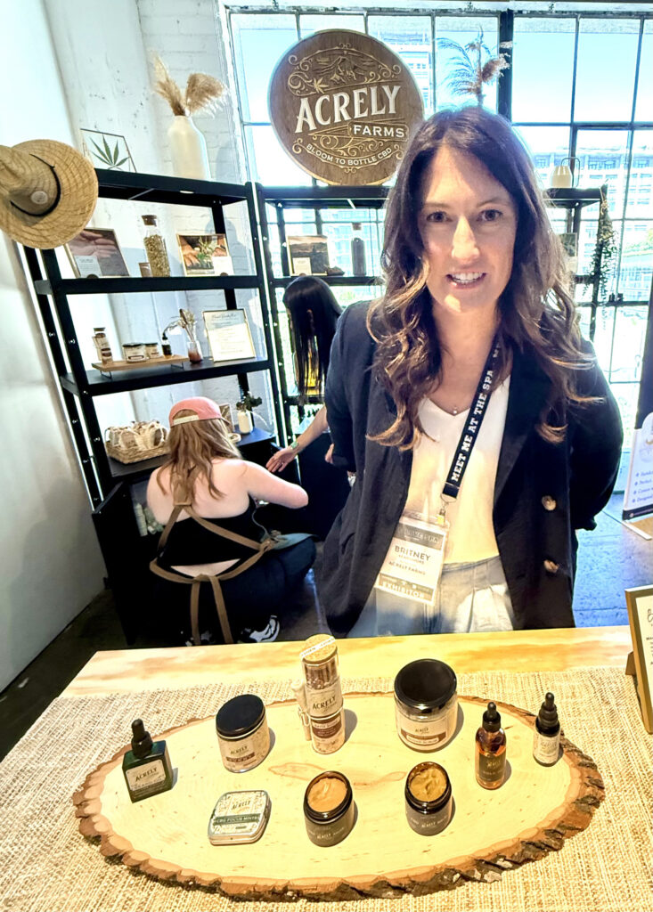 Woman in front of a product display with two female assistant behind her at the Acrely Farms booth at Live Love Spa LA 2025
