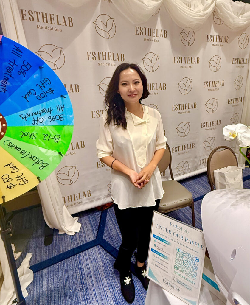 Woman in front of Esthelab Medical Spa banner with spin to win wheel and raffle QR code